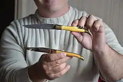 photographie. Un homme présente deux couteaux lagiole ouverts (dont un muni d'un tirebouchon