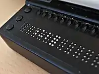 Photographie zoomant sur les premiers caractères d’une plage braille.